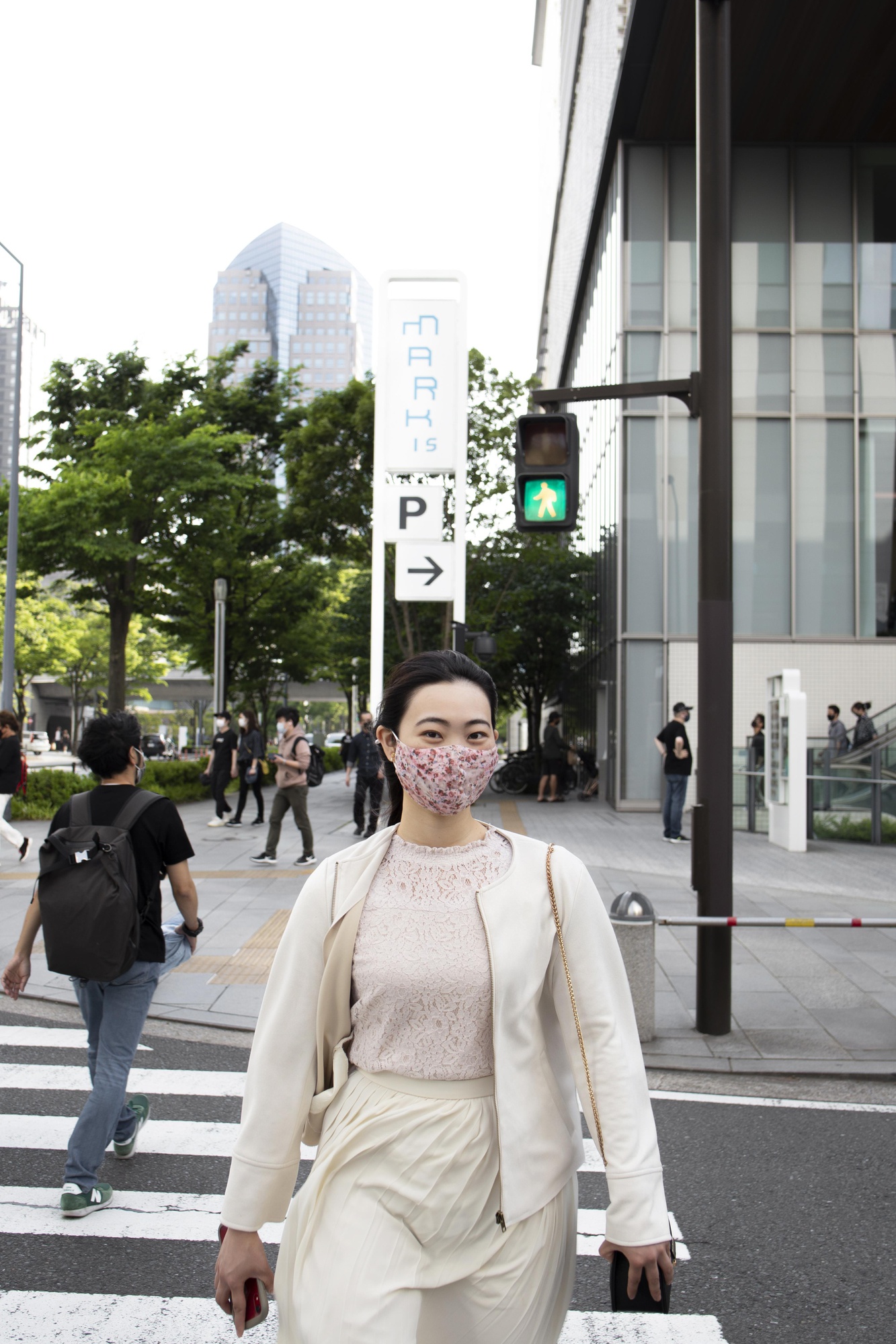 クリーム色の服装の女性が、近代的なビジネス街の通りを渡っている